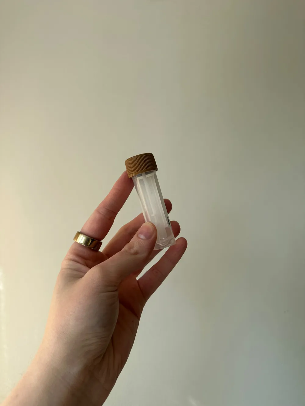 Hand houdt een buisje voor ontlastingsonderzoek vast tegen een lichte muur